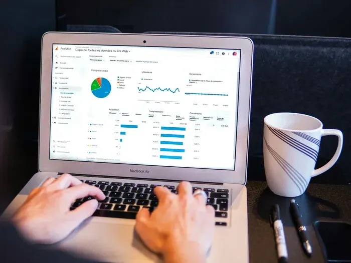 Hands working on a laptop showing graphs and reports from a web analytics dashboard beside a coffee mug on Town Service Today